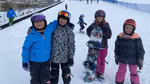 A group of diverse children learning to ski and snowboard.