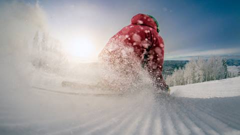 Skier skiing down a groomed trail in the sunshine at Steamboat Resort.