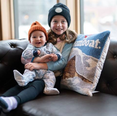 A young girl and baby smiling in Steamboat branded gear.